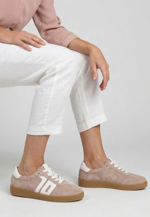 Person iført lyserøde ruskindssneakers med hvide snørebånd og detaljer, kombineret med hvide cropped bukser og en lyserød langærmet top.