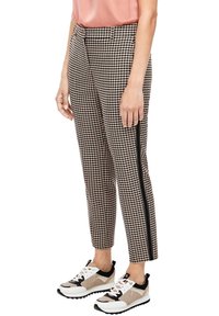 Pantalons à motif pied-de-poule noir et blanc avec une coupe slim, rayure sur le côté et tissu texturé, associés à des baskets épaisses.