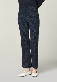 Mörkblå byxor med vita prickar, tillverkade av mjuk tyg, med rak passform och elastisk midja, i kombination med vita platta skor.