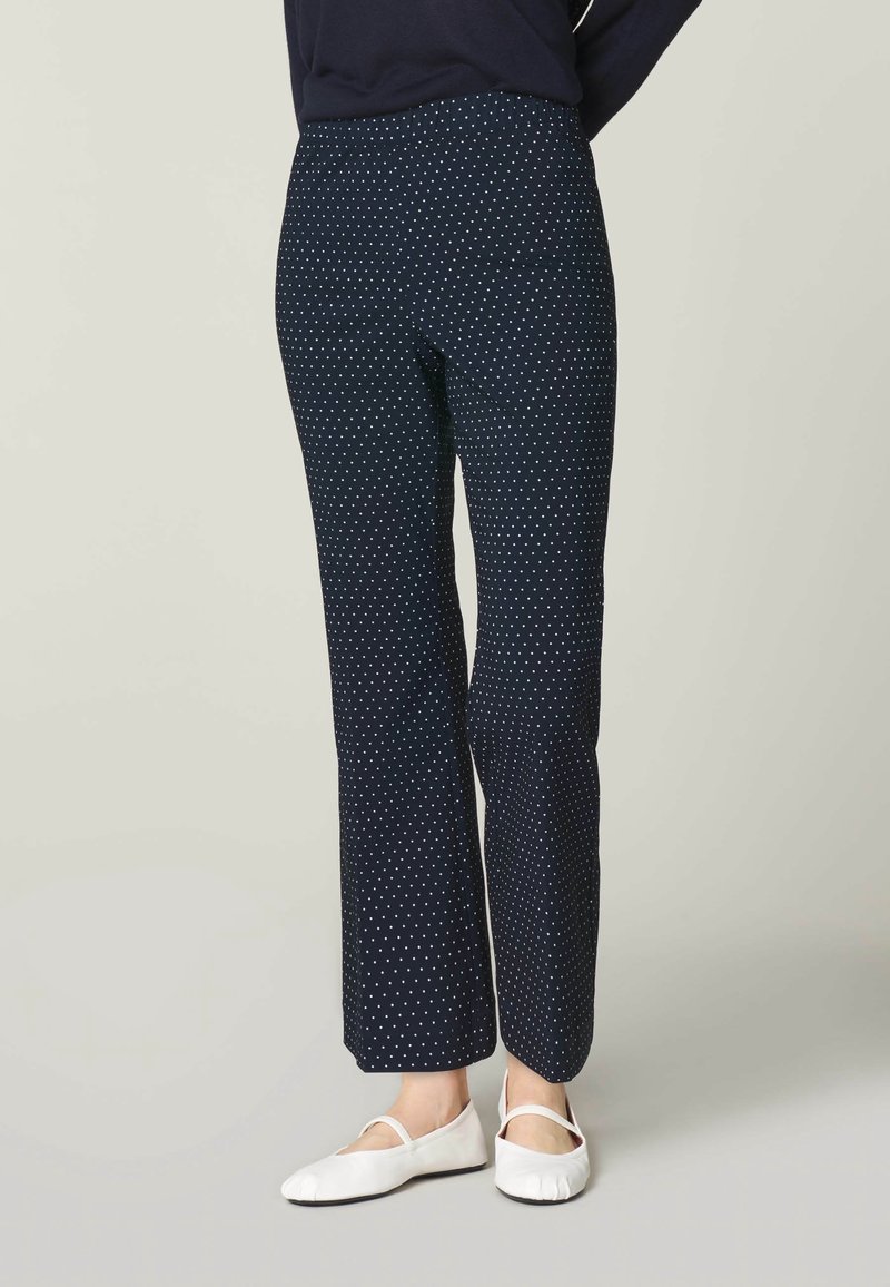 Mörkblå byxor med vita prickar, tillverkade av mjuk tyg, med rak passform och elastisk midja, i kombination med vita platta skor.