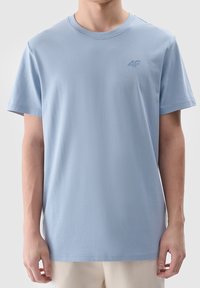 Jasnoniebieska krótka koszulka z miękkiej bawełny. Okrągły dekolt i małe, tonowe logo na lewej piersi. Gładka tekstura.