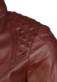 Bruine leren jas met een gestructureerde schouder en verhoogde diamanten studs, een gladde body en zichtbare stikseldetails.