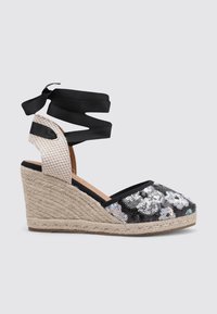 Espadrille de cuña con parte superior negra que presenta detalles florales de lentejuelas, suela de yute y cintas para el tobillo en negro. Tela texturizada y acentos tejidos.