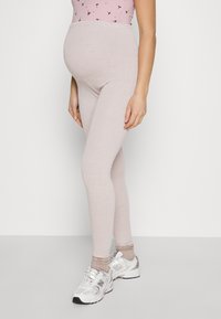 Light pink maternity leggings with a stretchy waistband, smooth texture, and fitted design, paired with white sneakers and beige socks.