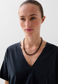 Czarna koszulka z dekoltem w serek zestawiona z naszyjnikiem z koralików, który składa się z okrągłych, błyszczących czarnych koralików, tworząc gładki, jednolity wzór.