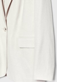 Blazer sur mesure blanc cassé avec fermeture à un bouton et poche à rabat rectangulaire sur le côté droit.