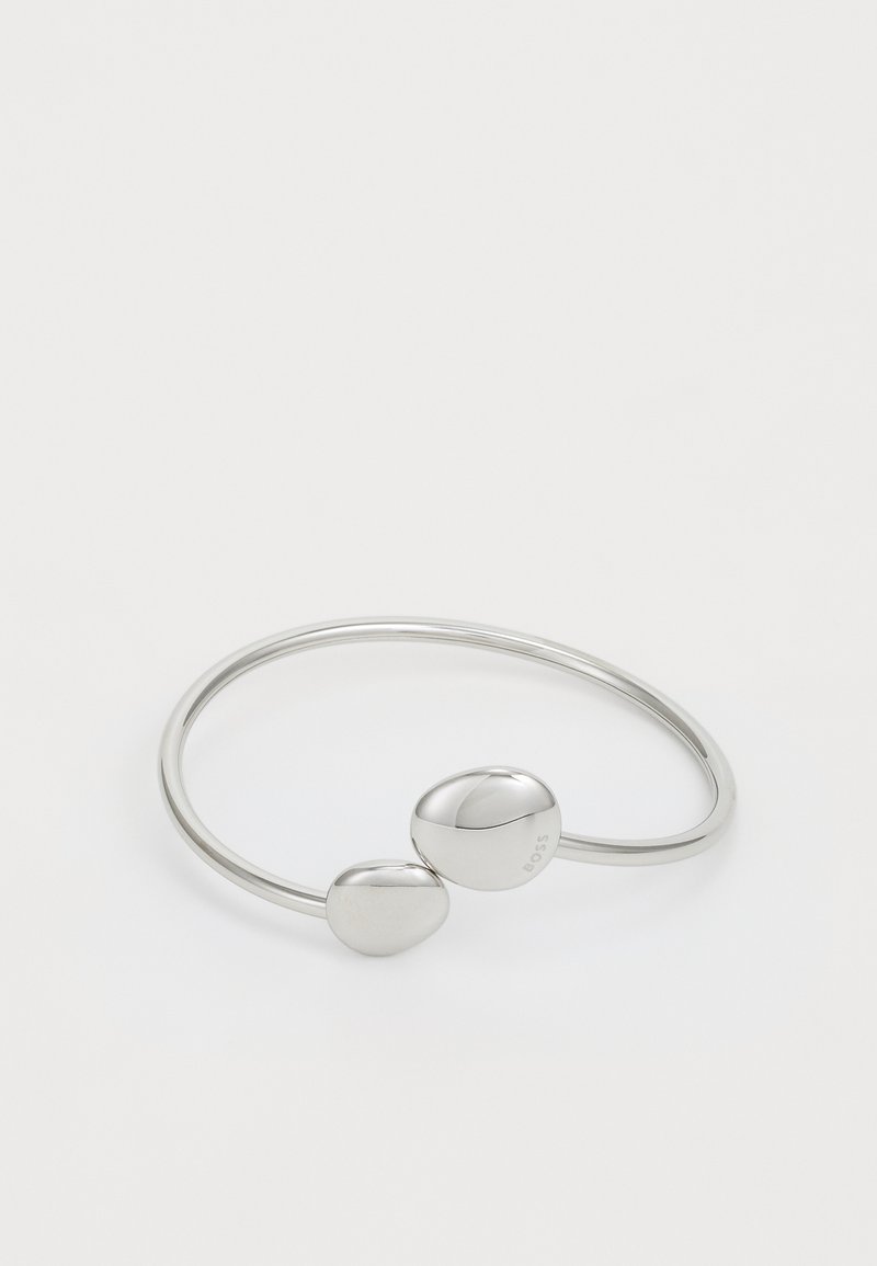 Srebrna zapestnica z minimalističnim dizajnom, ki vsebuje dva gladka, zaobljena akcenta. Narejena je iz poliranega kovine s preprosto odprto krožno obliko.