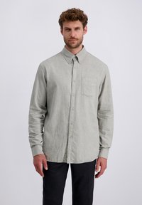 Camicia grigia chiaro a maniche lunghe con bottoni, realizzata in un tessuto testurizzato, dotata di una tasca sul petto e un colletto classico, abbinata a pantaloni scuri.