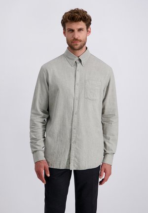 Camicia grigia chiaro a maniche lunghe con bottoni, realizzata in un tessuto testurizzato, dotata di una tasca sul petto e un colletto classico, abbinata a pantaloni scuri.