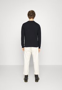 Maglione nero con maniche lunghe e collo rotondo, abbinato a pantaloni color crema, visto da dietro. Tessuto liscio, vestibilità casual.