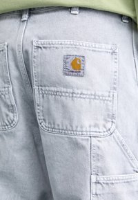 Šviesiai mėlyni džinsiniai kombinezonai su Carhartt prekės ženklo žyme. Paturtingi daugeliu kišenių, sustiprinta siūlėmis ir laisvos formos dizainas.