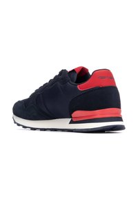 Baskets de sport bleu marine avec des matériaux en daim et en maille, accents rouges sur le talon et l'intérieur, semelle blanche et motif texturé sur la semelle extérieure.