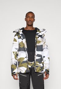 Kamuflázs dzseki fehér, szürke és olívazöld színekben, cipzáras elülső részel, kapucnival és texturált anyaggal. Fekete nadrággal párosítva, cipzáras zsebekkel.