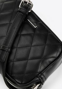 Sac bandoulière en cuir noir avec motif matelassé, quincaillerie en argent et sangle ajustable. Présente une texture lisse et une fermeture éclair.