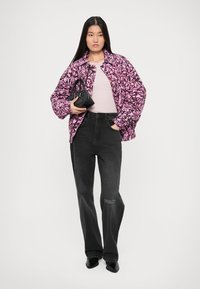 Pink floral-patterned puffer jacket, light pink shirt, black wide-leg jeans, and black handbag. Model wears black heeled shoes.