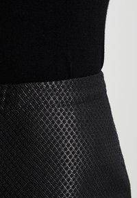 Top nero con una texture a maglia liscia, abbinato a una gonna nera con una texture e un motivo a diamante, creando un contrasto nei materiali.