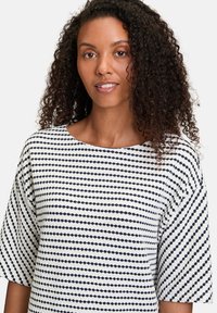 Top bianco con righe orizzontali blu navy, caratterizzato da un ampio scollo e maniche corte. Tessuto testurizzato con un motivo sottile.