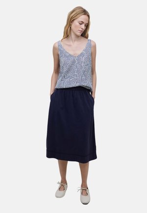 Falda larga azul marino con cinturilla fruncida, combinada con una blusa sin mangas de patrón geométrico en blanco y azul. Zapatos planos blancos.