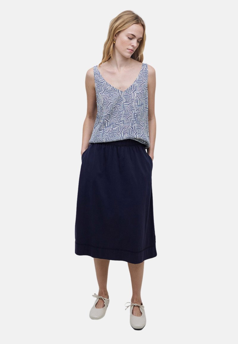 Falda larga azul marino con cinturilla fruncida, combinada con una blusa sin mangas de patrón geométrico en blanco y azul. Zapatos planos blancos.