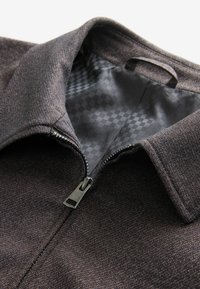 Dark brown jacket with a textured exterior, featuring a full zipper and a smooth, patterned interior lining. Collar design is classic.