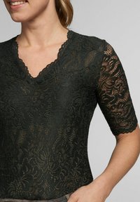 Schwarzes Spitzentop mit kurzen Ärmeln, V-Ausschnitt und floralem Muster. Das Design hat gewellte Kanten und eine taillierte Silhouette.