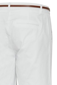 Pantalon blanc à coupe ajustée, avec poches latérales et une ceinture marron visible à la taille.