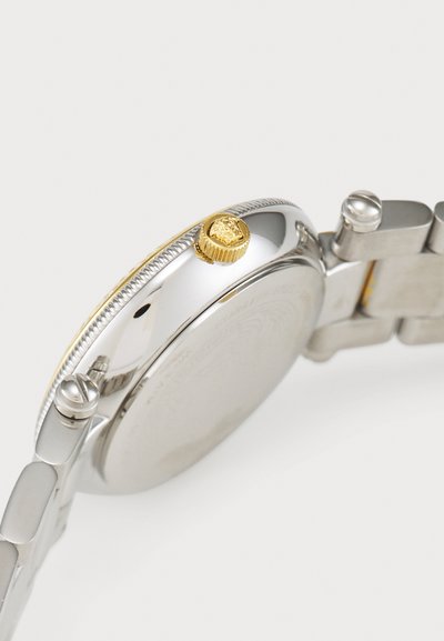 Silver metal wristwatch features a textured bezel and a golden crown. The bracelet has polished links with a matte finish on the case back.