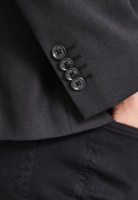 Black blazer sleeve with four black buttons, featuring a textured fabric and stitched details. The cuff is tailored with a slim fit.