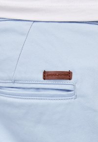 Poche de pantalon bleu clair avec fente horizontale et petite étiquette en cuir marron cousue au-dessus avec texte de marque embossé.