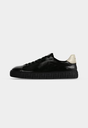 Czarny niski sneaker z czarną wzorzystą podeszwą i białą zakładką na pięcie, widziany od strony zewnętrznej na jednolitym jasnym tle.