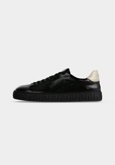 Μαύρο sneaker χαμηλής κοπής με μαύρη μοτίβο σόλα και λευκό ταμπελάκι στη φτέρνα, φαίνεται από την εξωτερική πλευρά σε απλό φωτεινό φόντο.