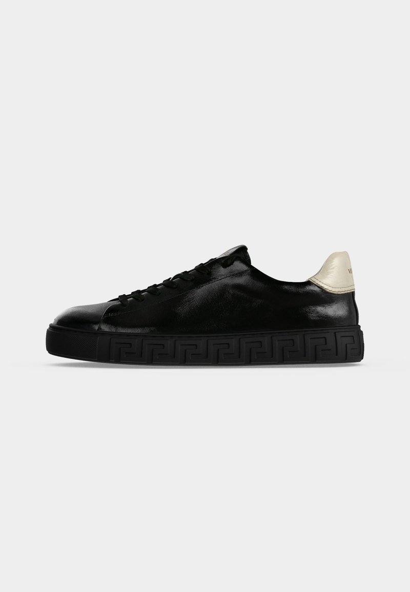 Schwarzer Sneaker in niedriger Ausführung mit schwarzer, gemusterter Sohle und weißem Fersenlasche, von der Außenseite auf einfarbig hellem Hintergrund gesehen.