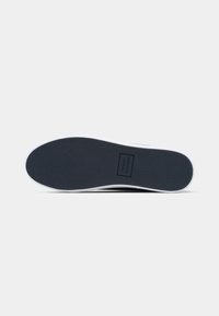 Semelle d'une sneaker bleu marine avec des bordures blanches, arborant le logo Tommy Hilfiger embossé au centre de la semelle.