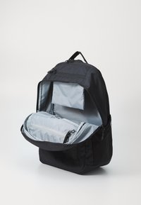 Schwarzer Rucksack mit einem Reißverschluss, grauem Innenraum, mehreren Fächern, darunter eine Netztasche und ein gepolstertes Fach für Gegenstände.