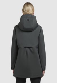 Zwarte waterdichte jas met een capuchon, voorzien van een aansluitende bovenkant en een uitlopende onderkant, zichtbare stiksels en knoopdetails op de mouwen.
