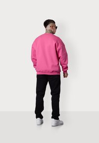 Sweatshirt rose avec col rond et épaules tombantes, associé à un pantalon noir et des baskets blanches ; possède un tissu texturé.