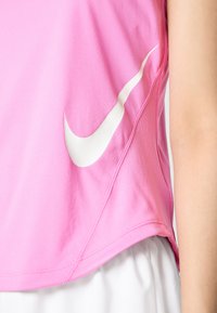 Roza atletska majica bez rukava napravljena od laganog materijala, s bijelim Nike logotipom i mrežastim detaljima duž ruba za prozračnost i udobnost.