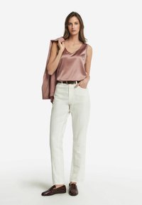 Sukienka satynowa w kolorze mauve, białe dżinsy z wysokim stanem i ciemnobrązowe mokasyny. Modelka trzyma dopasowaną marynarkę na jednym ramieniu. Minimalistyczny, czysty wygląd.