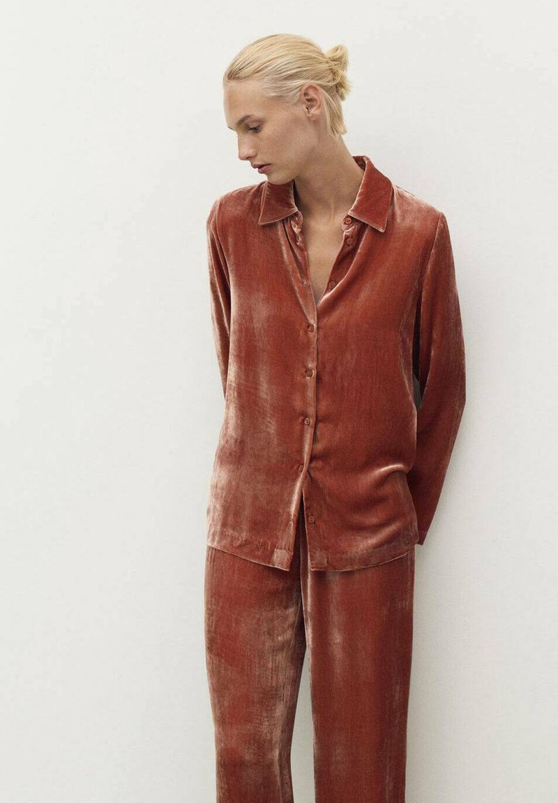 Set di pigiama in velluto color ruggine, composto da una camicia a bottone con colletto e pantaloni abbinati, caratterizzati da una finitura morbida e testurizzata e una vestibilità rilassata.