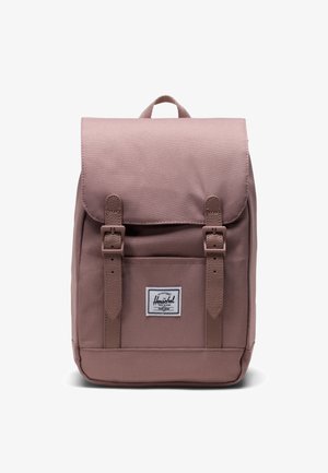 Zaino rosa chiaro realizzato in tessuto testurizzato, con chiusura a pattina, due spallacci regolabili e una toppa con logo sul fronte. Design robusto e strutturato.