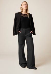 Dopasowana czarna marynarka z cekinowymi akcentami, zestawiona z czarnym teksturowanym topem i szerokimi szarymi spodniami, uzupełniona czarnymi butami.