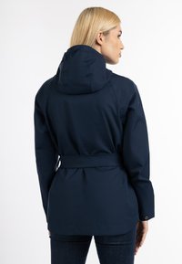 Jachetă impermeabilă de culoare albastru închis, cu glugă, având talie cu curea, buzunare laterale și manșete elastice. Textură netedă și moale, cu detalii minime.