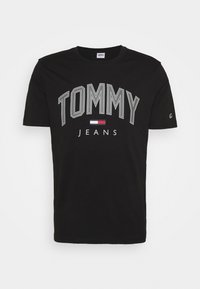 Czarny bawełniany t-shirt z napisem "TOMMY" dużymi szarymi literami oraz "JEANS" mniejszymi białymi literami, z małym akcentem w postaci francuskiej flagi.