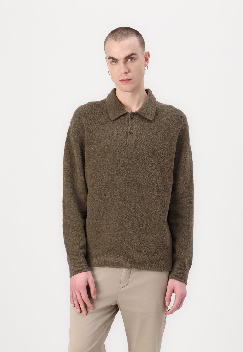 Brauner, strukturierter Pullover mit Kragen und einer Knopfleiste mit drei Knöpfen. Lange Ärmel und gerippter Saum, kombiniert mit hellbeigen Hosen.