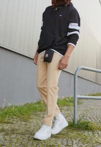Black hooded sweatshirt with white stripes, beige pants, and white sneakers. Contains a black pouch attached to the waist.