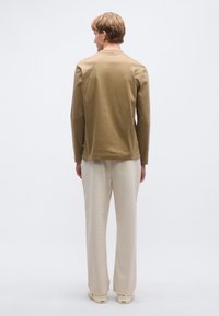 Hosszú ujjú barna pamut ing laza szabással, világos bézs széles szárú nadrággal és krémszínű tornacipővel párosítva, hátulnézetben.