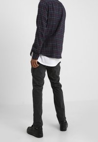 Geruite flanellen overhemd in marineblauw en bordeaux met een gebogen zoom, gedragen over een witte T-shirt met ronde hals. Donkergrijze cargobroek en zwarte sneakers.