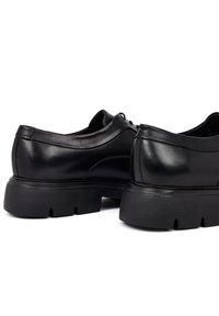 Zwarte leren schoenen met een ronde vorm, voorzien van een dikke, gestructureerde rubberen zool en subtiele stiksels op de zijkanten.