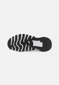 Suela de zapato atlético en blanco y negro con goma texturizada para agarre, que presenta canales prominentes y un diseño robusto para tracción y soporte.
