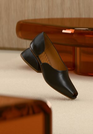 Black leather open-toe heeled shoes with a low, angled heel and smooth texture. The insole features a subtle zigzag pattern.